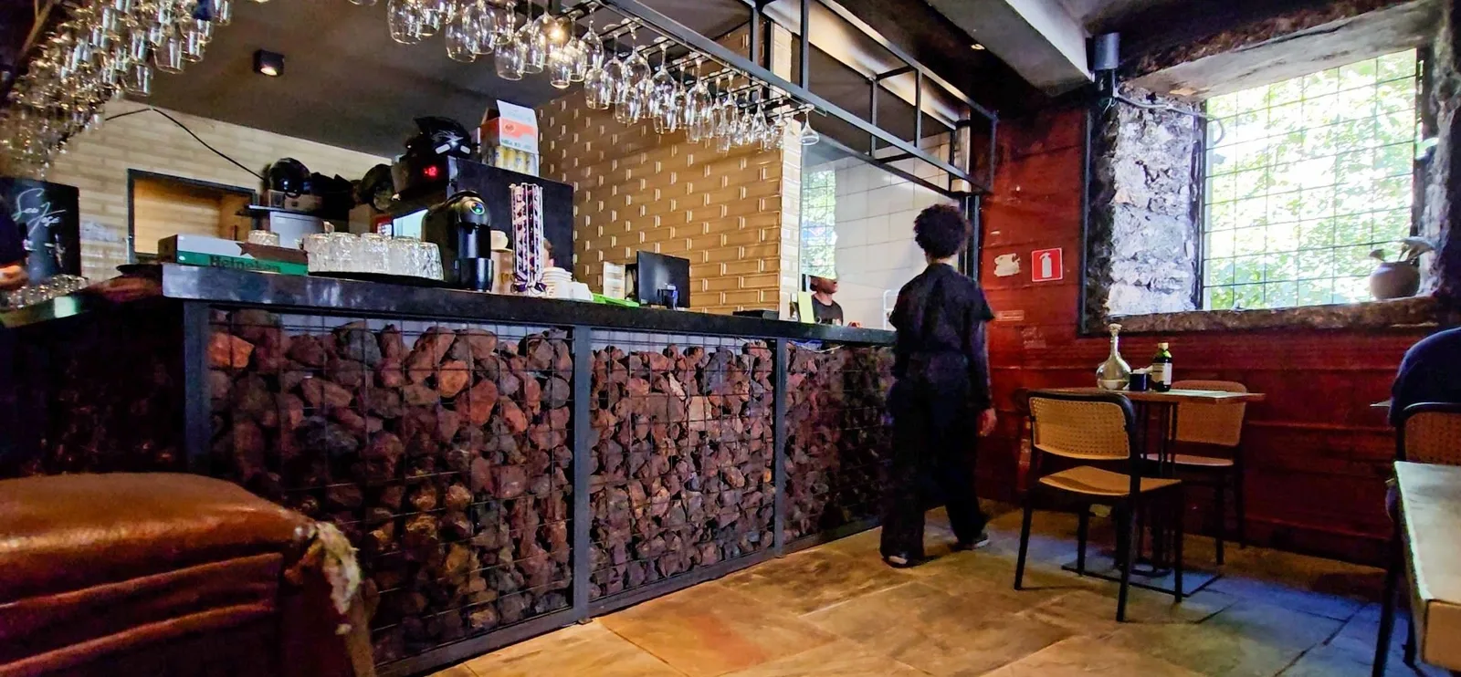 Balcão do bar revestido de pedras de minério, taças penduradas e parede de azulejo